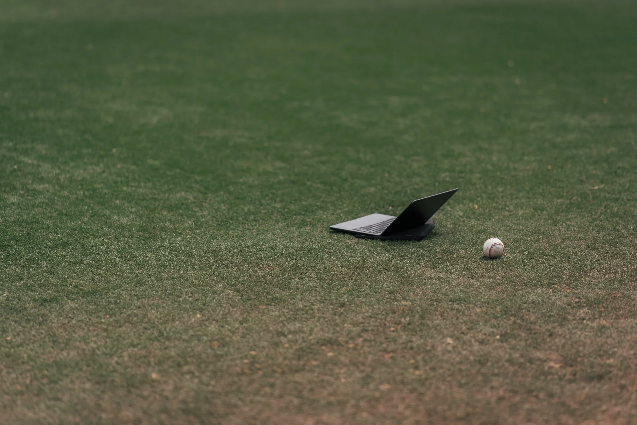 Laptop and baseball on outfield grass